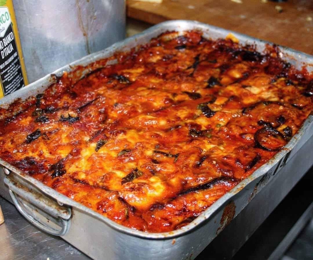Today I am telling you about a southern dish that everyone loves: the perfect Apulian eggplant parmigiana.  It is not known exactly where this dish originated; some say in Sicily and then in Campania, but it is very popular and made all over the South.  The original “Bari-style” version involves a filling of provolone, mozzarella and mortadella.  The essential element for the success of this dish is absolutely the quality of the raw materials.  1) The eggplants recommended for this dish are the long, purple ones with a slightly bitter flavor. Ideally, to eliminate the bitterness slightly, salt the sliced eggplant with a heavy weight on top, such as a press, so that they release some liquid and do not absorb too much oil during frying.  2) Cut the eggplant lengthwise only, no more than 0.2 inch thick. Never make them round. I have to say that in the South eggplants are dipped in flour and then in egg, so the original recipe is like that, but I honestly prefer them without egg and flour, just fried. Your choice.  3) To prevent water from wetting the parmigiana during cooking, it is best to salt it first. Once sliced, stack them, sprinkle them with coarse salt and let them rest for a little more than an hour with a heavy weight on top. Of course, before frying them, rinse and dry them a bit. This procedure will also help to slightly remove the bitterness of the oblong eggplants.  Continued on the next page  ADVERTISEMENT  Next→